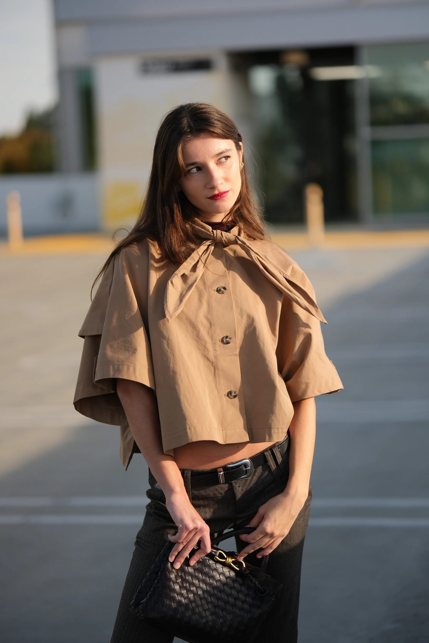 Rosina half body holding a woven bag in front of a modern building — photo B