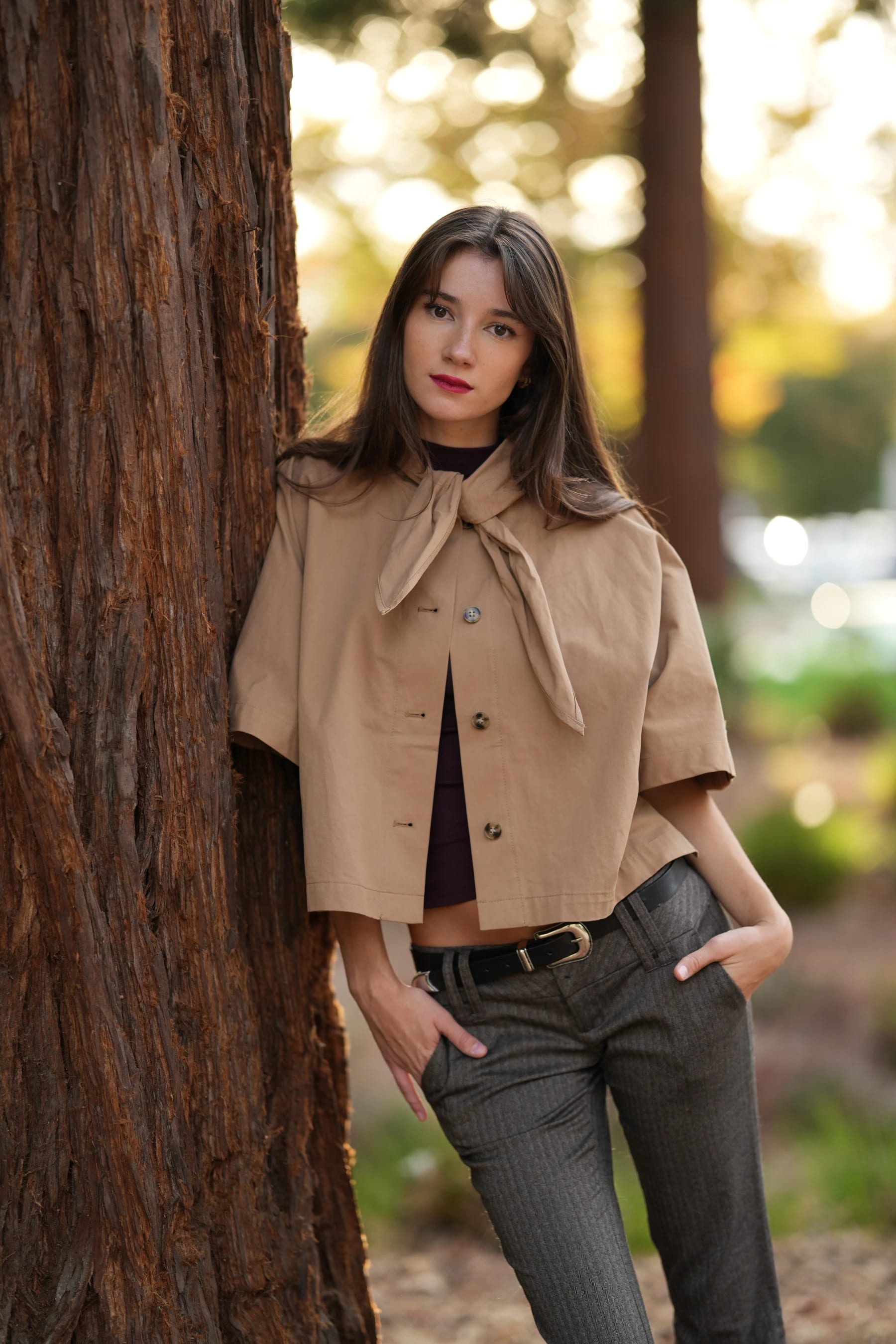 Rosina leaning on a redwood trunk with her hands in her pockets — photo B