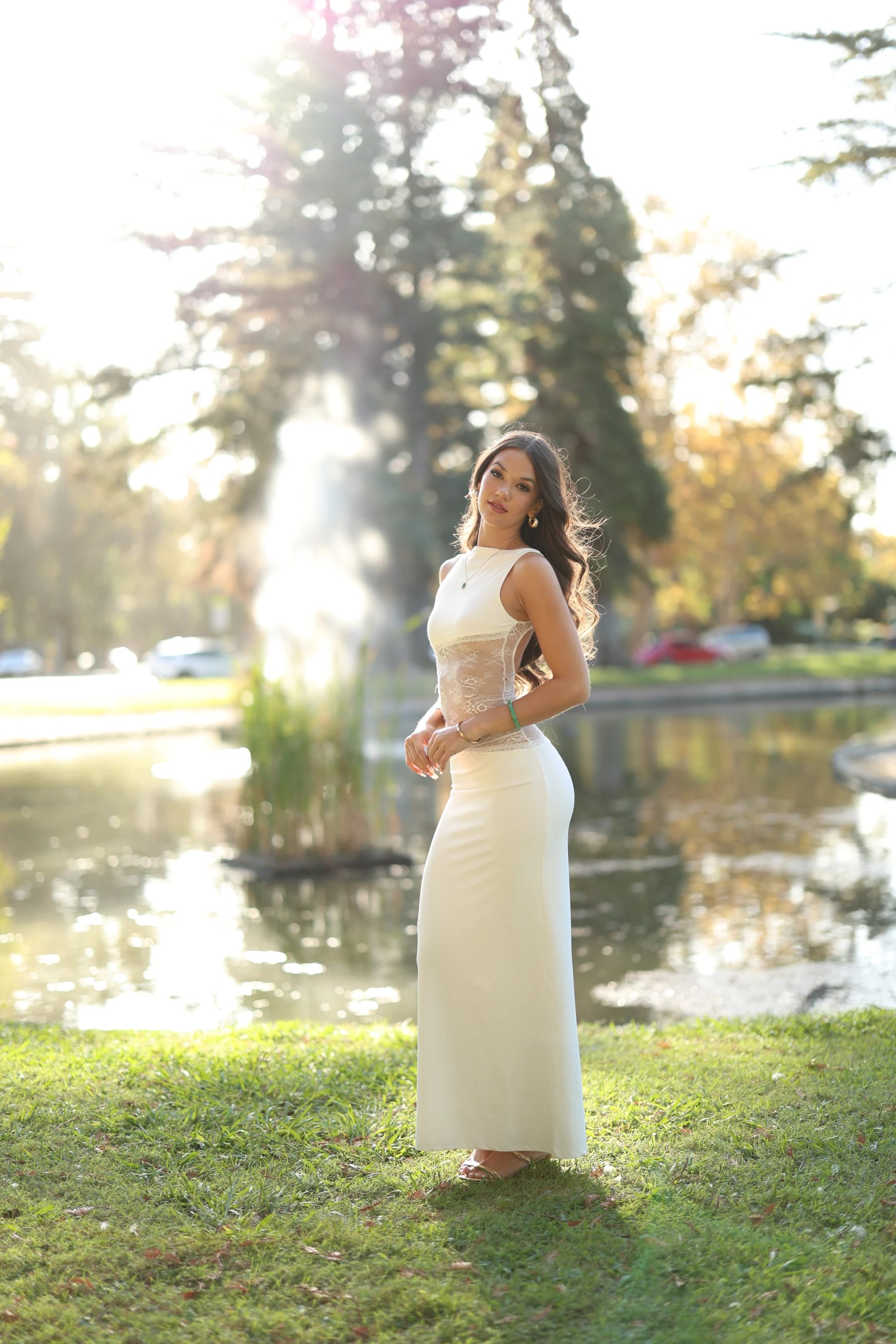 Mia full length by the pond with the fountain behind her — photo B