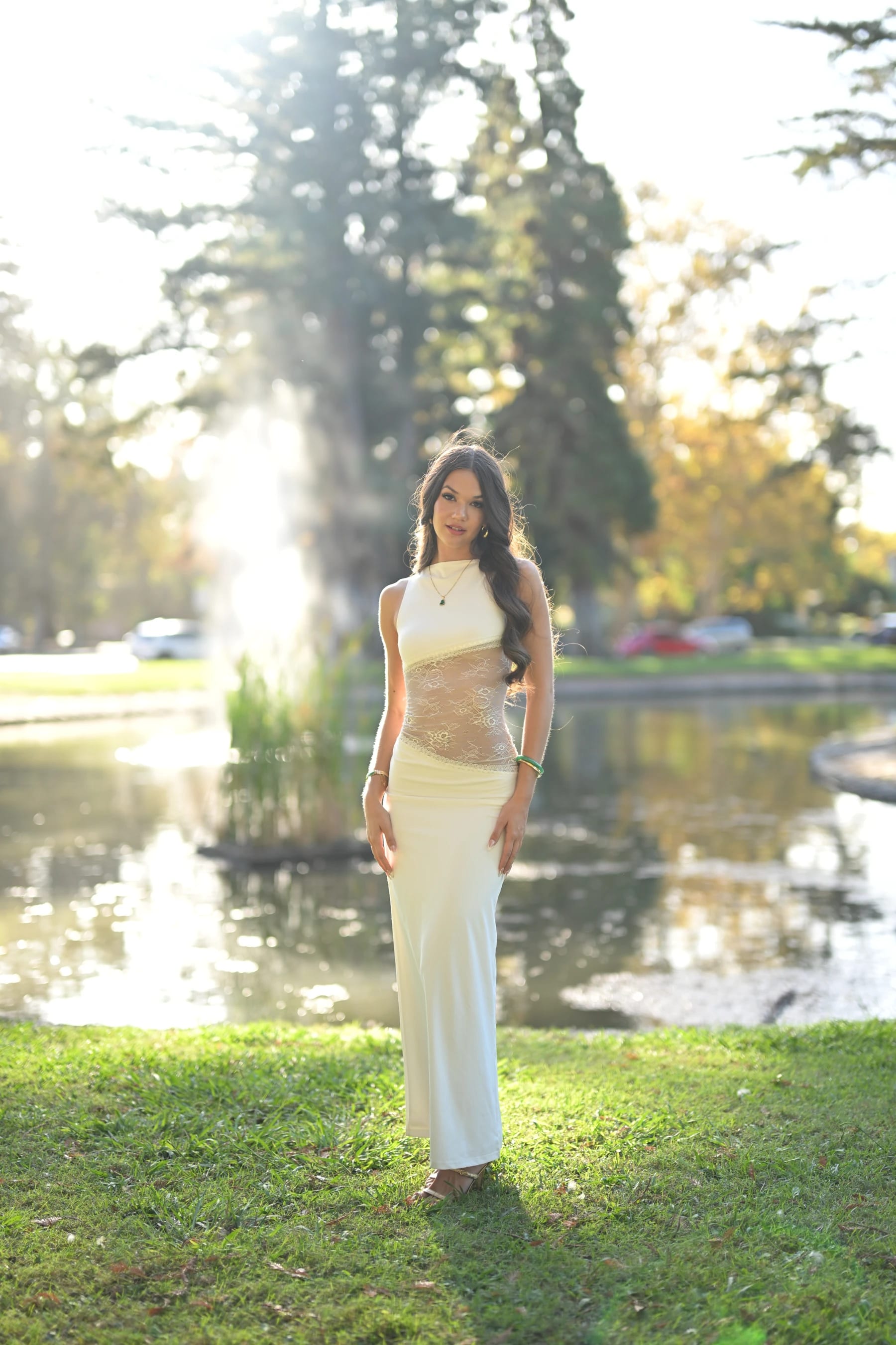 Mia full length by the pond with the fountain behind her — photo A