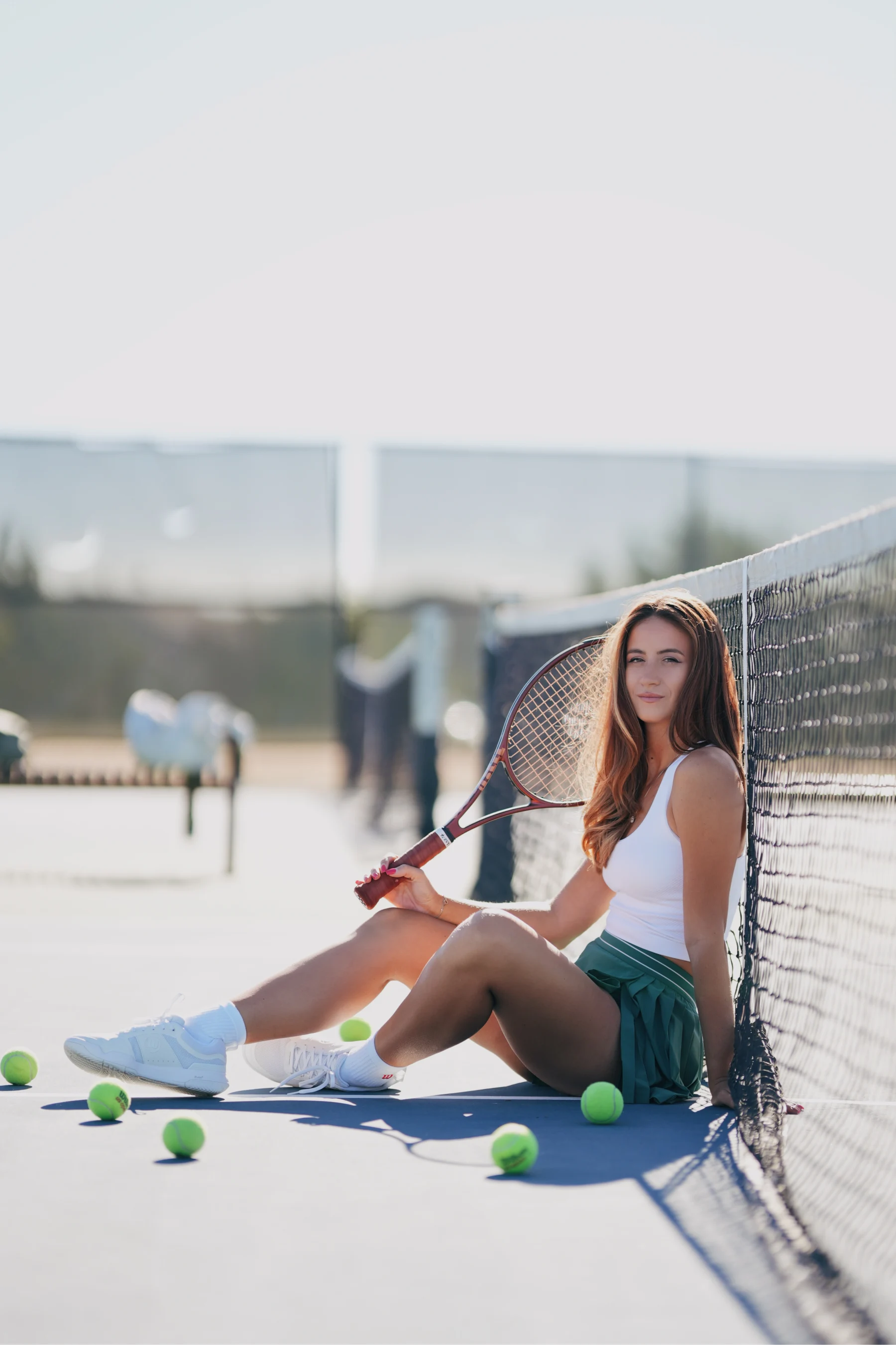 Natalia seated courtside in a green tennis skirt, tennis balls scattered, soft early morning light